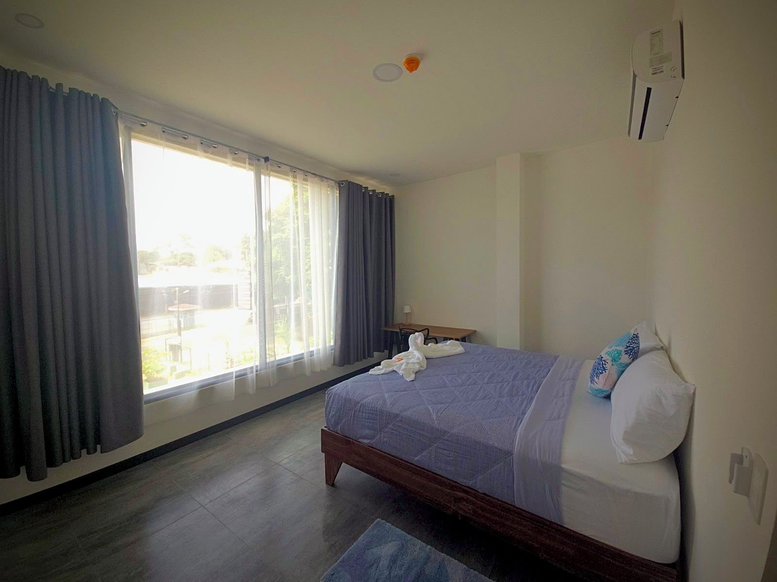 A hotel room with a bed, a desk, and a window with curtains.