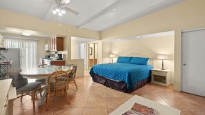 Quarto de hotel com cama, escrivaninha, cadeira, mesa de jantar e cozinha compacta.
