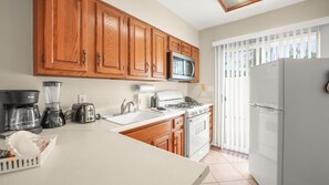 A kitchen with wooden cabinets, a microwave, a stove, and a refrigerator. - Sunshine State of Mind | Palm Springs Studio (Palm Springs)