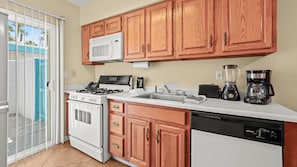 A kitchen with wooden cabinets, a stove, microwave, sink, and coffee maker. - Palm Springs Poolside Escape that Sleeps 4 (Palm Springs)