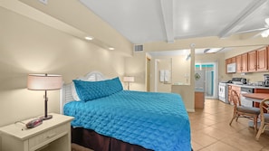 A hotel room with a bed, bedside table, lamp, and a view into the kitchen area. - Palm Springs Poolside Escape that Sleeps 4 (Palm Springs)