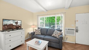 A living room with a sofa, a coffee table, a TV, and a window with blinds. - Palm Springs Poolside Escape that Sleeps 4 (Palm Springs)