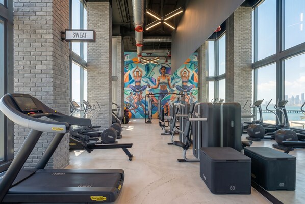 A gym with treadmills, weight machines, and a mural of people exercising. - Luxury Skyline Studio in Downtown Miami (Miami)