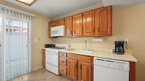 A compact kitchen with wooden cabinets, a microwave, a gas stove, a coffee maker, and a dishwasher. - Desert Charm & Fireside Comfort (Palm Springs)