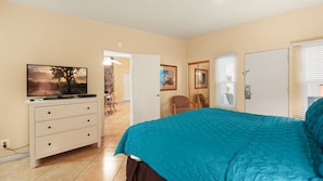 A bedroom with a bed, a dresser, a television, and a door leading to another room. - Desert Charm & Fireside Comfort (Palm Springs)