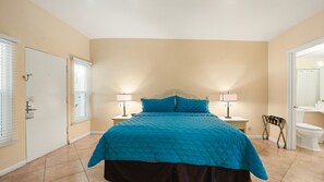 A bedroom with a bed, two bedside lamps, a door, and a toilet. - Desert Charm & Fireside Comfort (Palm Springs)