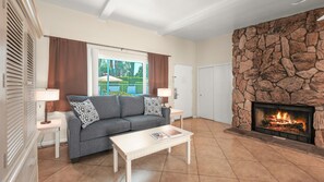 A living room with a stone fireplace, a sofa, a coffee table, and a view of the outdoors. - Fireside Palm Springs Escape | 1BR + 2 Baths (Palm Springs)