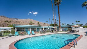 A pool area with lounge chairs and umbrellas, a building with a blue roof, and palm trees. - Fireside Palm Springs Escape | 1BR + 2 Baths (Palm Springs)