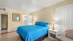 Ein Hotelzimmer mit Bett, Nachttisch, Stuhl und einer Tür zum Badezimmer.