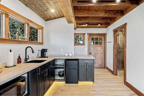 A modern kitchen with a wooden ceiling, built-in appliances, and a large window. - A-frame • Hot Tub • Sauna • Outdoor Shower (Penrose)