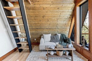 A cozy interior with a wooden wall, a sofa, a coffee table, and a window. - A-frame • Hot Tub • Sauna • Outdoor Shower (Penrose)