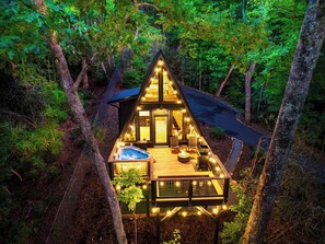 A triangular wooden cabin with a hot tub and deck, surrounded by trees. - A-frame • Hot Tub • Sauna • Outdoor Shower (Penrose)
