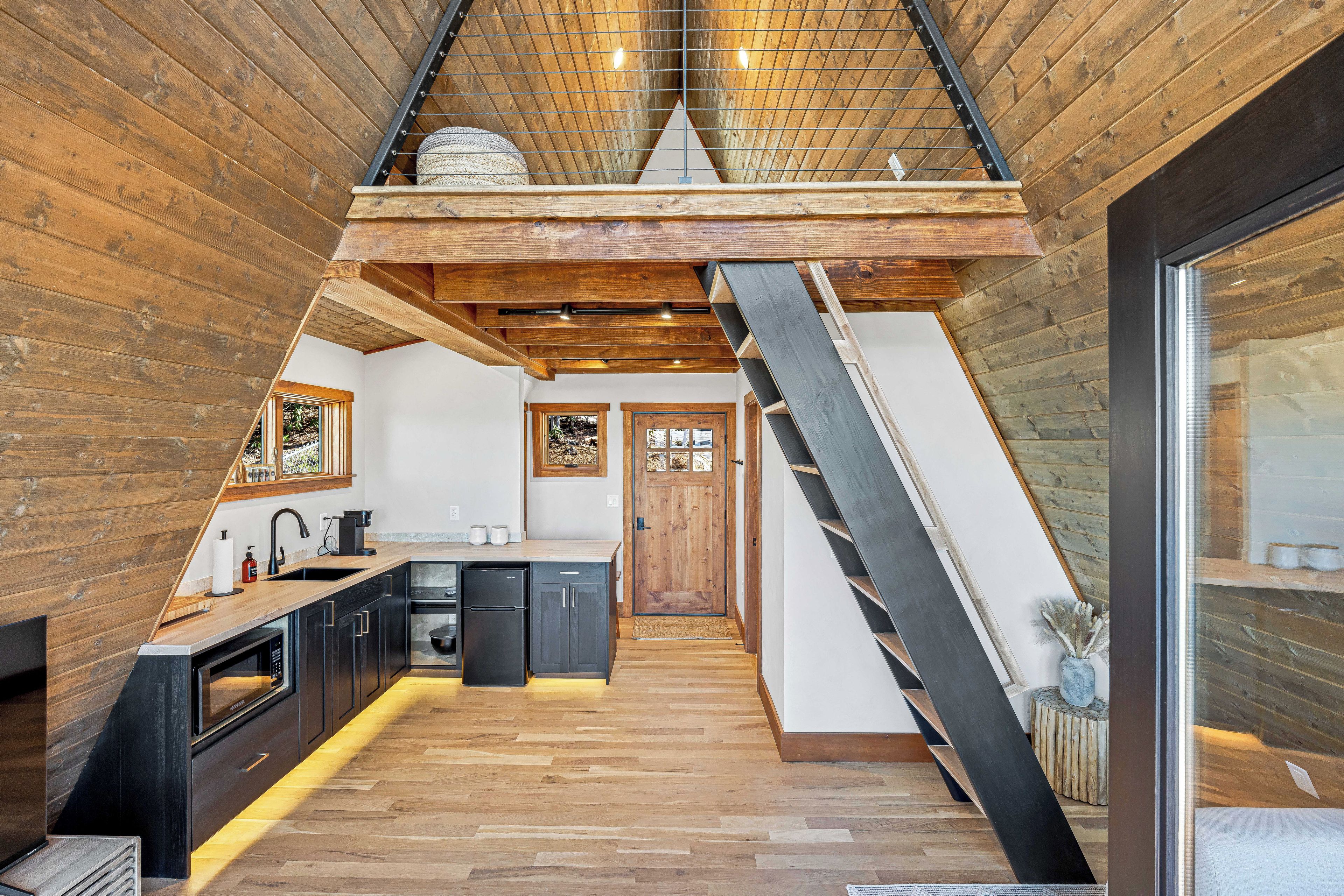A modern kitchen with a central island, wooden flooring, and a sloped ceiling with exposed beams.
