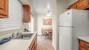 A kitchen with a white refrigerator, wooden cabinets, a sink, and a dining area with chairs. - 1 Bedroom for Palm Springs Adventures (Palm Springs)