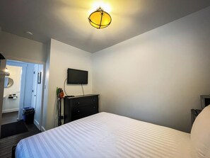 Une chambre d’hôtel avec un lit, une commode, un téléviseur fixé au mur et une porte donnant sur une salle de bain.