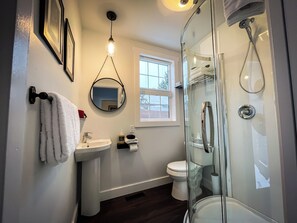 Une salle de bain avec une douche à parois de verre, un lavabo blanc, des toilettes et une serviette suspendue à un crochet.
