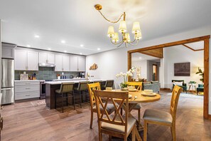 A modern kitchen with a central island, bar stools, and a dining table with chairs. - BourbonTrl Luxe-15acres-GolfSim-HotTub-GameRm (Versailles)