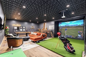 A modern indoor space with a pool table, comfortable seating, a large screen displaying a golf game, and a green artificial turf area. - BourbonTrl Luxe-15acres-GolfSim-HotTub-GameRm (Versailles)