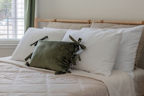 Ein Bett mit einem Holz-Kopfstück, weißer Bettwäsche und einem grünen Kopfkissen mit Schleifen.