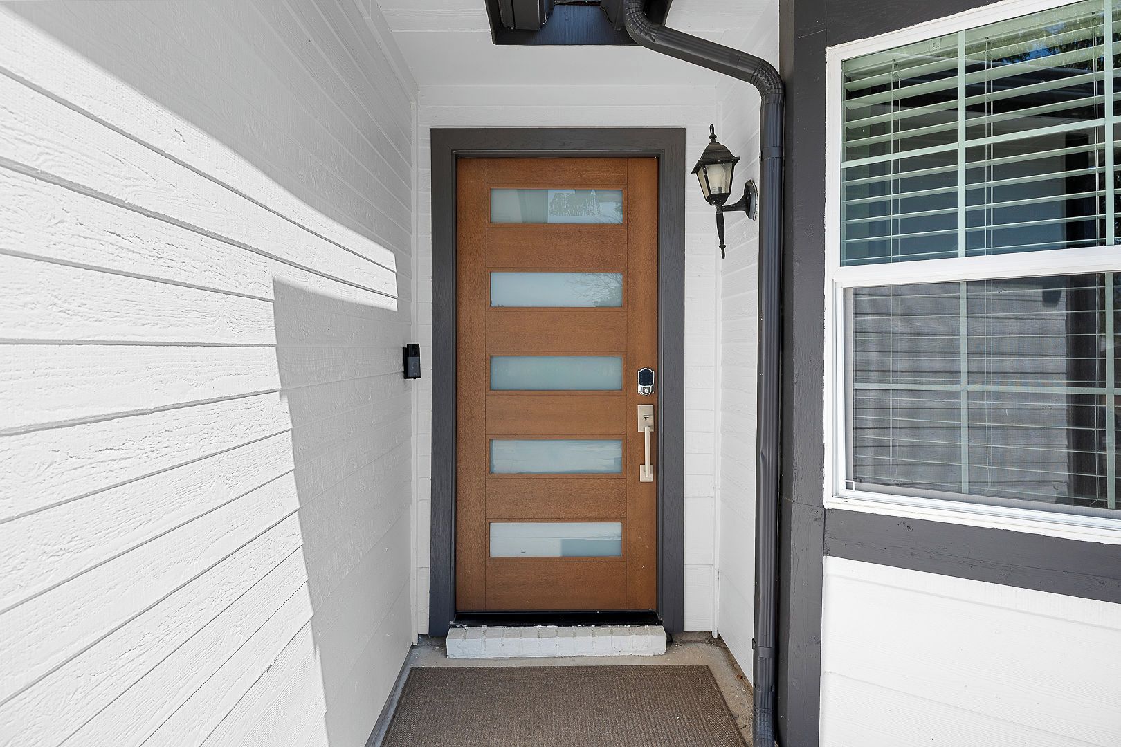 A white exterior wall with a wooden door featuring frosted glass panels and a metal handle.
