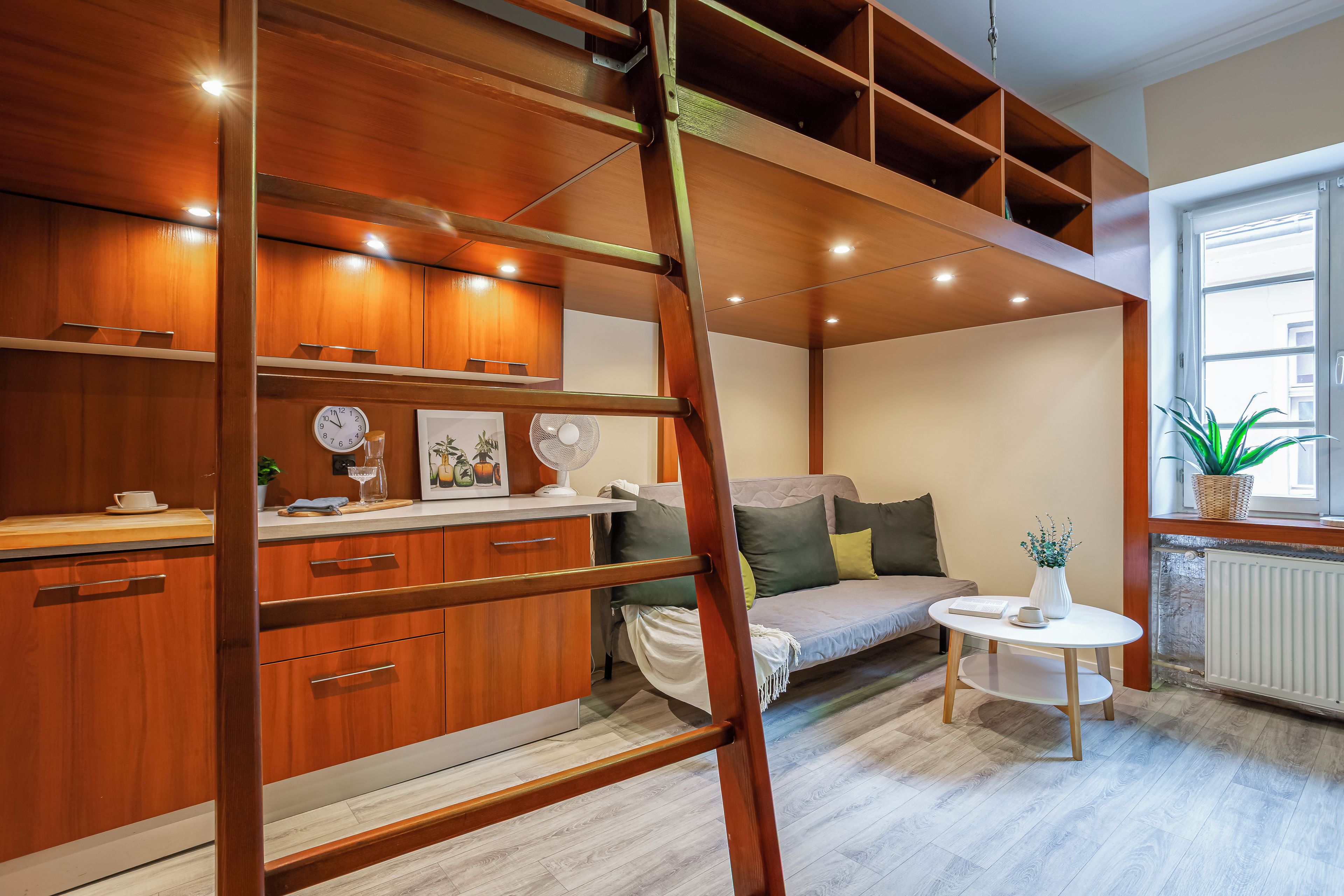 Une chambre moderne de style loft, dotée d’un lit en mezzanine, d’étagères en bois intégrées, d’une petite table ronde et d’une fenêtre offrant une vue agréable.