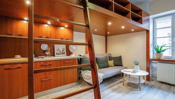 Una habitación moderna estilo loft con cama elevadas, estanterías de madera empotradas, una pequeña mesa redonda y ventana con vistas.