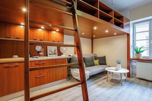Una habitación moderna estilo loft con cama elevadas, estanterías de madera empotradas, una pequeña mesa redonda y ventana con vistas.