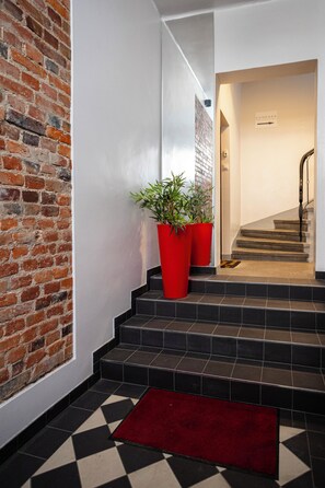 A staircase with black tiles and a red carpet leading to a door with a sign. - Studio z Antresolą 1 min od Rynku (Poznań)