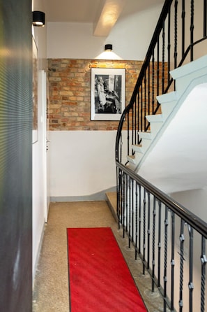 Una escalera con alfombra roja que sube, un muro de ladrillo y un cuadro enmarcado encima de los escalones.