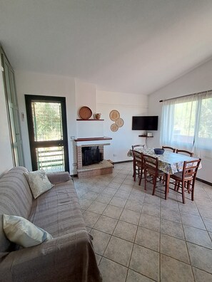 A living room with a sofa, a fireplace, a dining table with chairs, and a television. - Solanas_A cozy and relaxing villa with plenty of outdoor space (Cuili Murvoni)