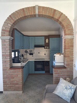 A kitchen with blue cabinets, a brick archway, and a microwave on the countertop. - Solanas_A cozy and relaxing villa with plenty of outdoor space (Cuili Murvoni)
