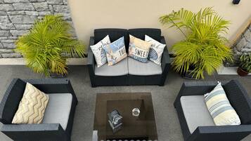 A patio with a sofa set, two side tables, and potted plants.