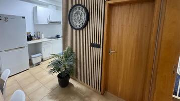 Een moderne keuken met witte kasten, een Samsung koelkast, een houten wandpaneel met een klok en een potplant.