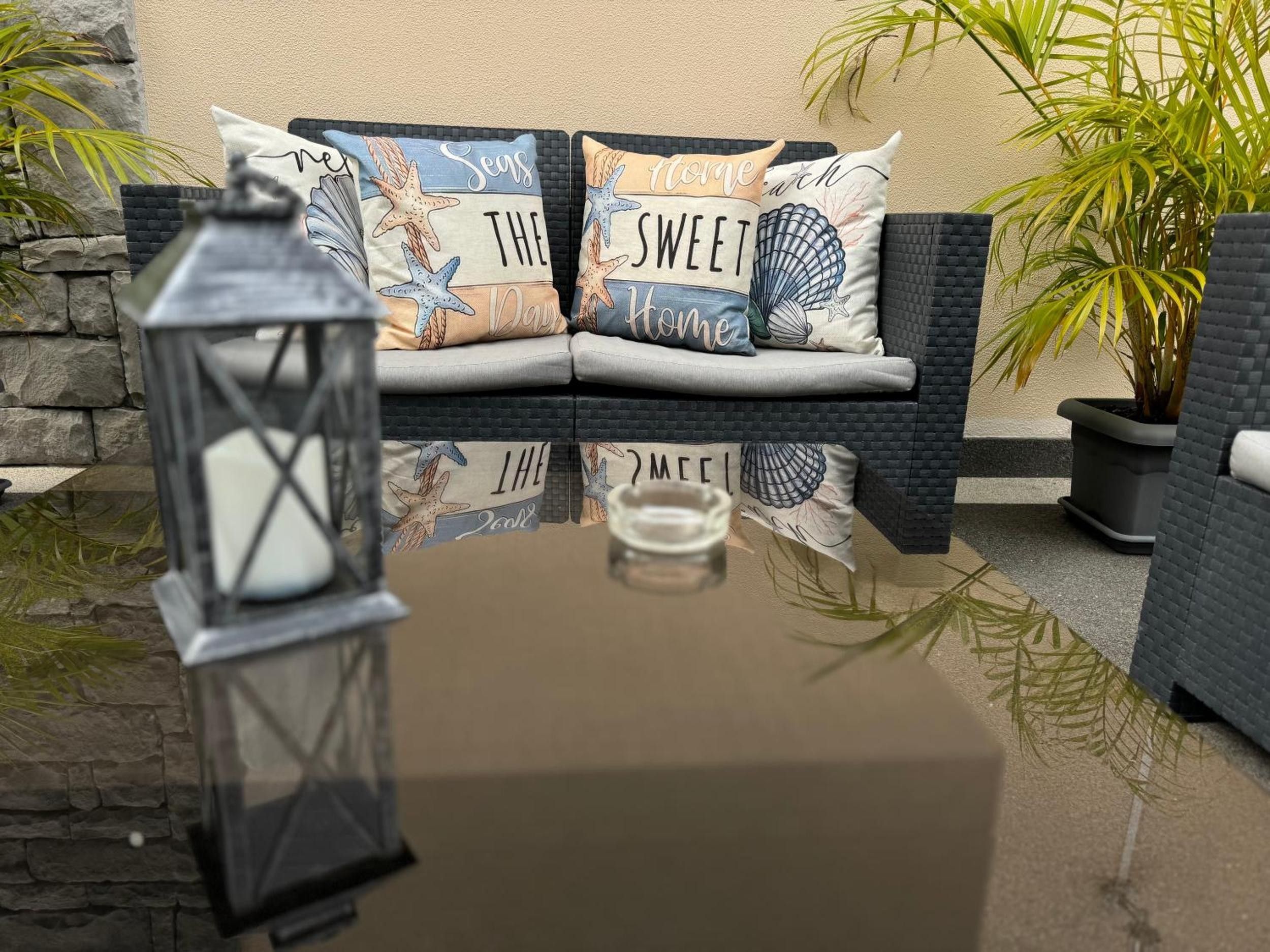 A cozy outdoor seating area with a stone wall, a wicker sofa, and decorative pillows with nautical themes.