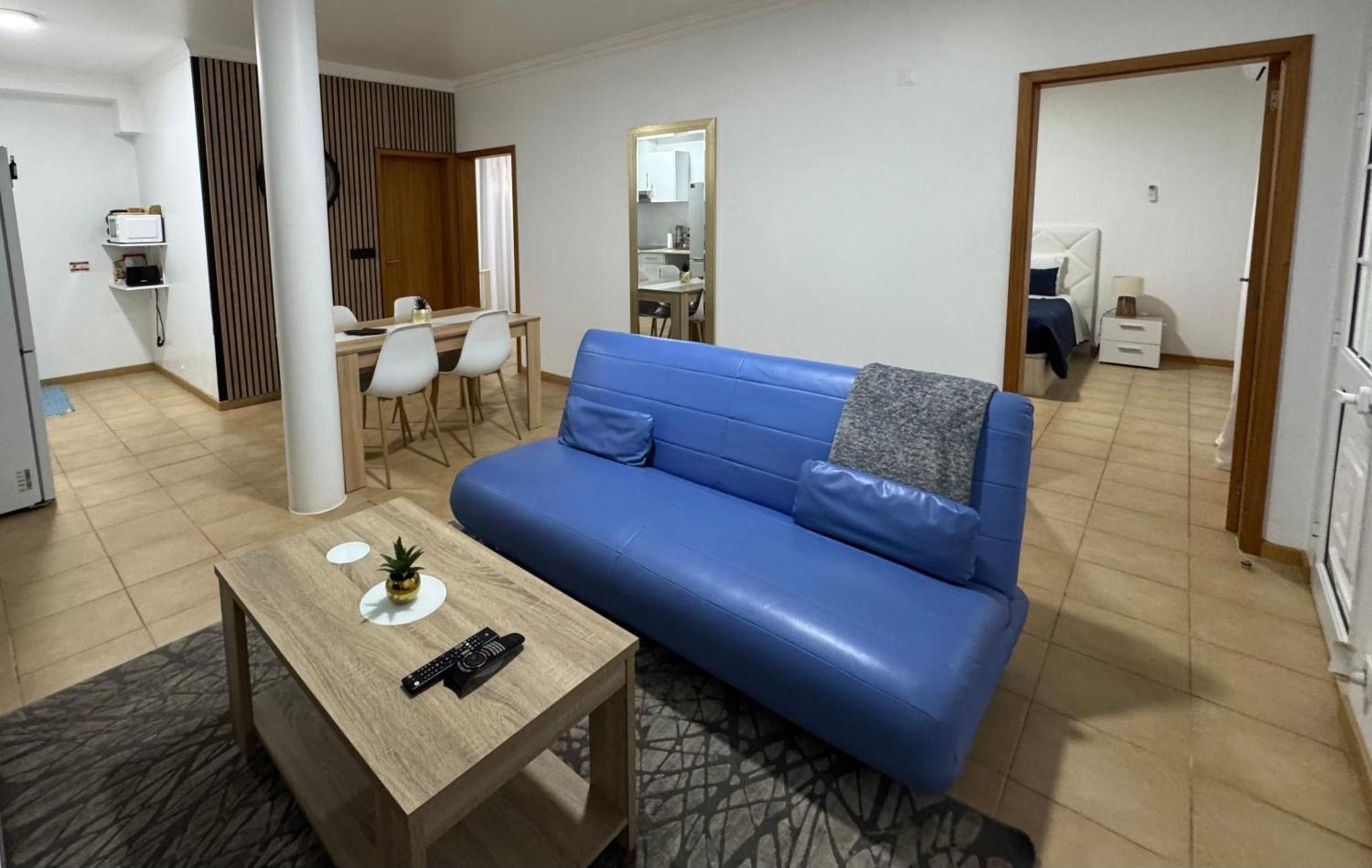 Ein modernes Wohnzimmer mit einem blauen Sofa, einem Holztisch und einem Essbereich mit weißen Stühlen.