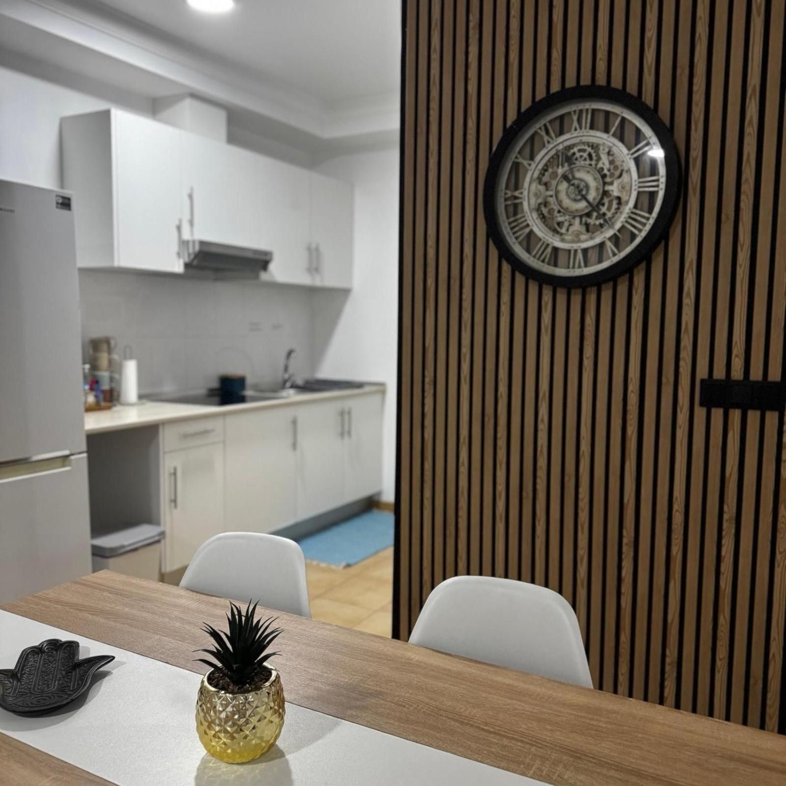 Eine moderne Küche mit weißen Schränken, einer Uhr an der Wand und einem Esstisch mit Stühlen.
