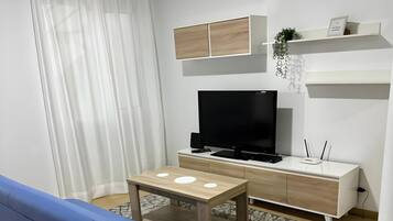 Un salon moderne avec un canapé bleu, une table basse en bois, un téléviseur à écran plat et un coin repas blanc comprenant une table et des chaises.