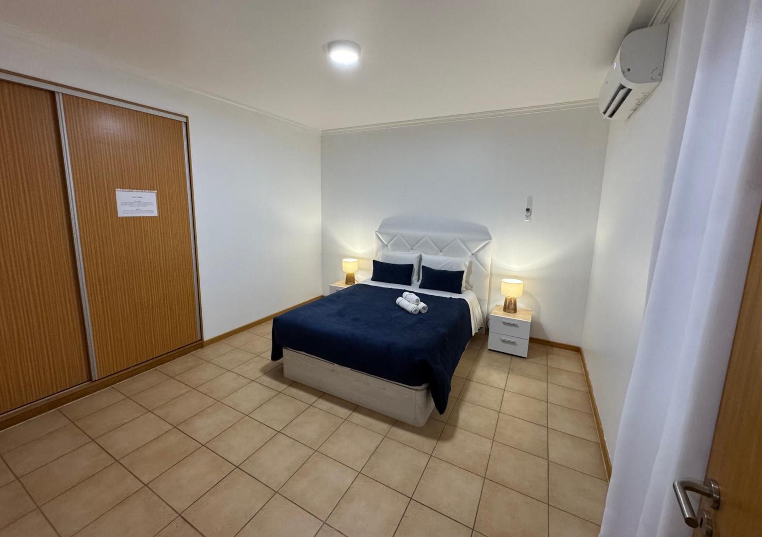 Une chambre à coucher avec un lit, des tables de chevet, une armoire et un luminaire au plafond.