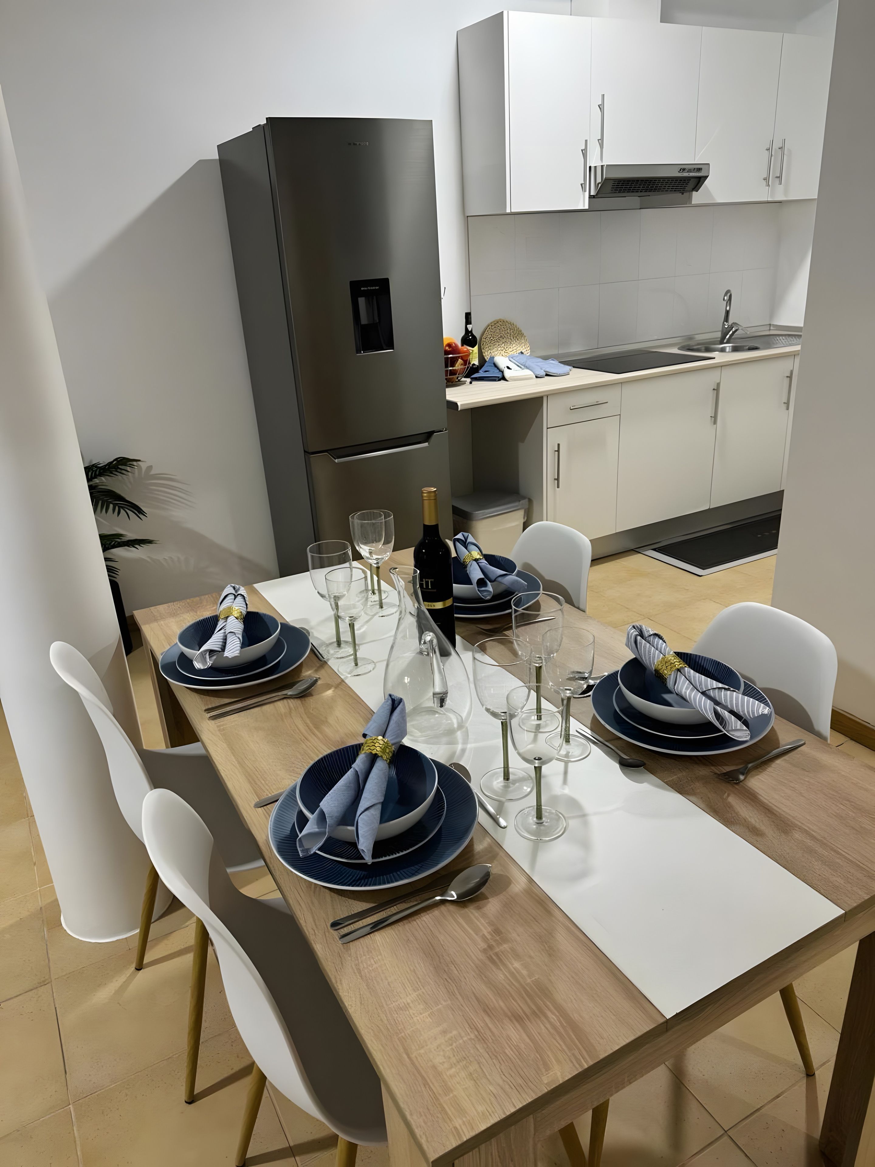 Een moderne keuken met witte kastjes, een inbouwoven en een eethoek voor zes personen, compleet met witte stoelen en een houten tafel.