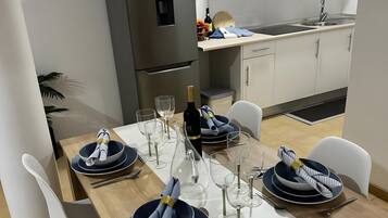 Een moderne keuken met witte kastjes, een inbouwoven en een eethoek voor zes personen, compleet met witte stoelen en een houten tafel.