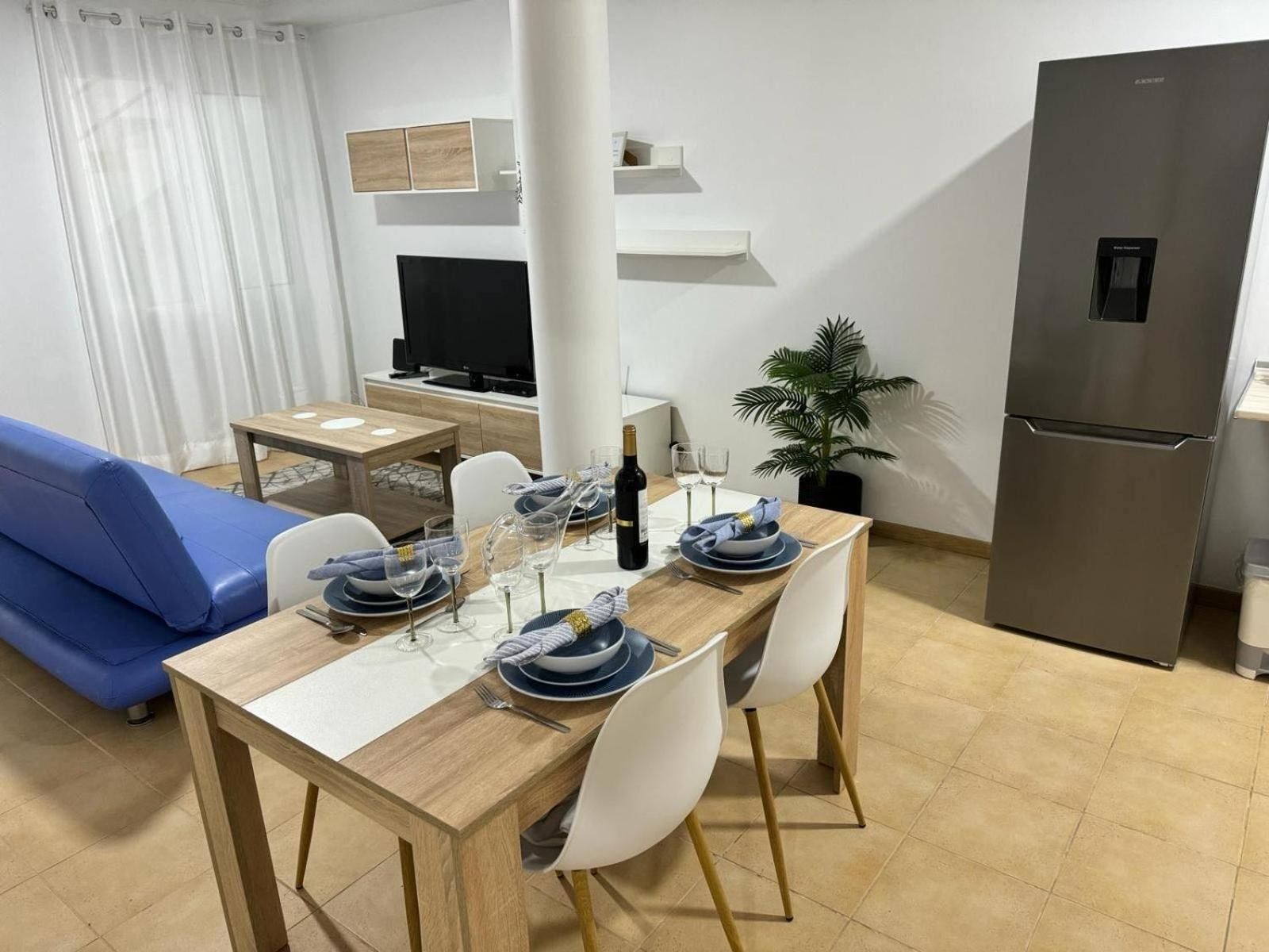 Une cuisine moderne avec une table à manger pour quatre personnes, un canapé bleu, un téléviseur et un réfrigérateur.