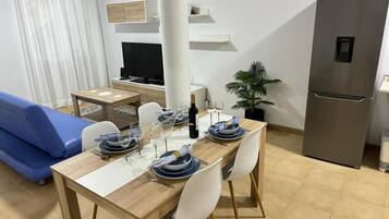 Une cuisine moderne avec une table à manger pour quatre personnes, un canapé bleu, un téléviseur et un réfrigérateur.
