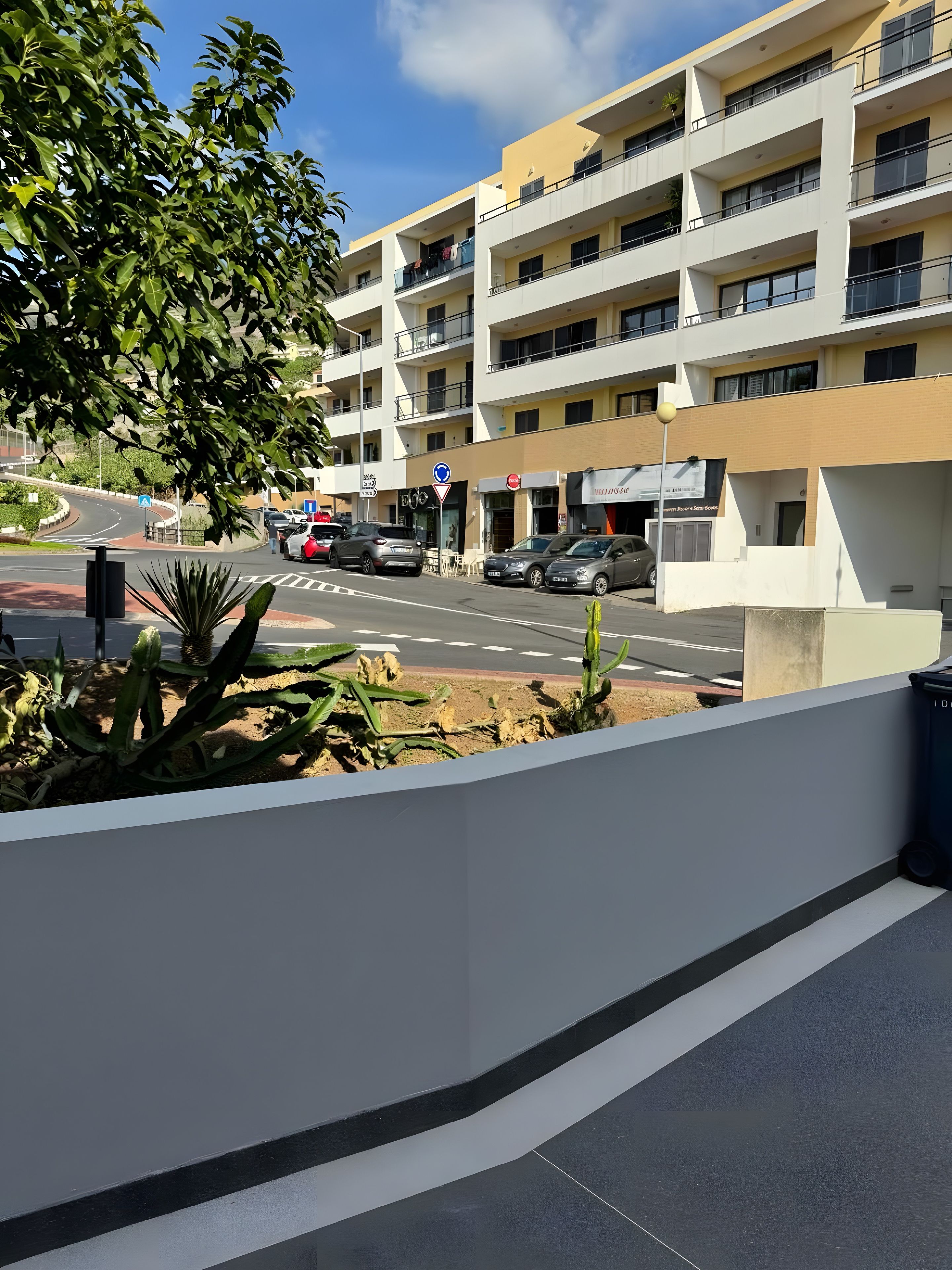 Ein mehrstöckiges Gebäude mit Balkonen, eine Straße mit Autos und ein klarer Himmel.