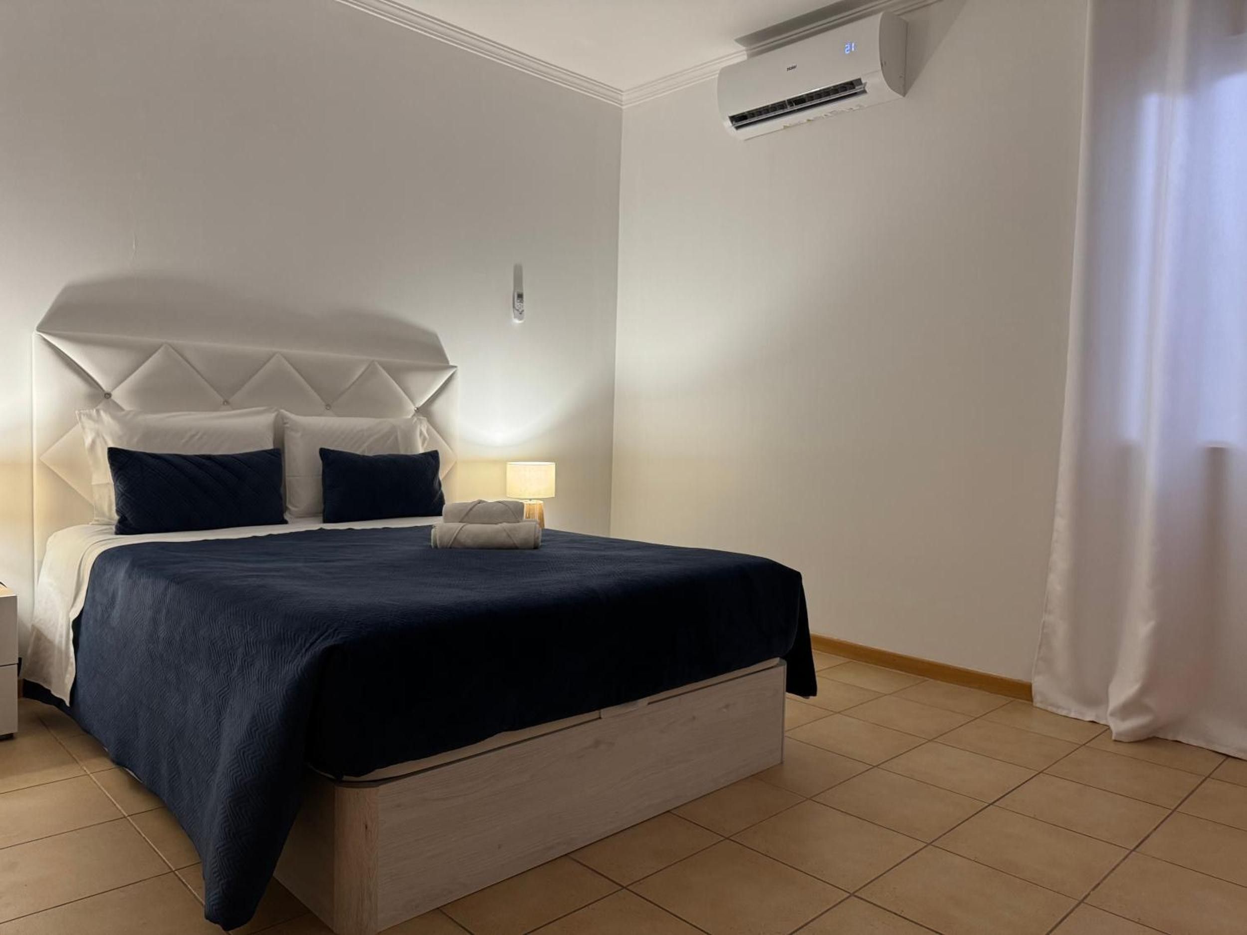 Una habitación de hotel con una cama, una mesita de noche, una lámpara y un equipo de aire acondicionado.