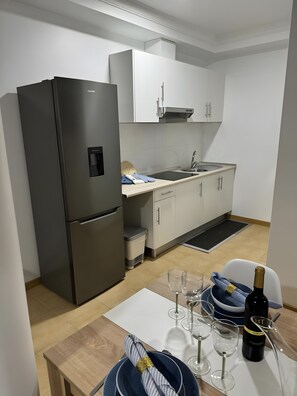 A modern kitchen with a black refrigerator, white cabinets, and a dining area with a table set for a meal. - Apartment 'Alforra Residence 1' with Mountain View, Wi-Fi and Air Conditioning (Câmara de Lobos)