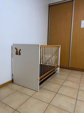 A room with a white crib, a wooden door, and a tiled floor. - Apartment 'Alforra Residence 1' with Mountain View, Wi-Fi and Air Conditioning (Câmara de Lobos)
