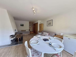 A dining area with a round table set for four, a sofa, a small cabinet, and a refrigerator. - Ground floor, balcony, tv, ski locker, 67m², Praz sur Arly (Praz-sur-Arly)