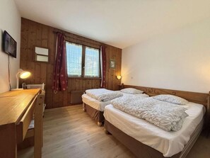 A room with two beds, a wooden desk, a radiator, and a window with curtains. - Ground floor, balcony, tv, ski locker, 67m², Praz sur Arly (Praz-sur-Arly)