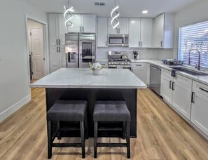 A modern kitchen with a central island, stainless steel appliances, and a large window. - Vegas Group Getaway | Private Pool & Grill (Las Vegas)