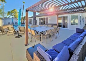 An outdoor patio with a pool, a covered dining area, and a seating area with cushions. - Vegas Group Getaway | Private Pool & Grill (Las Vegas)
